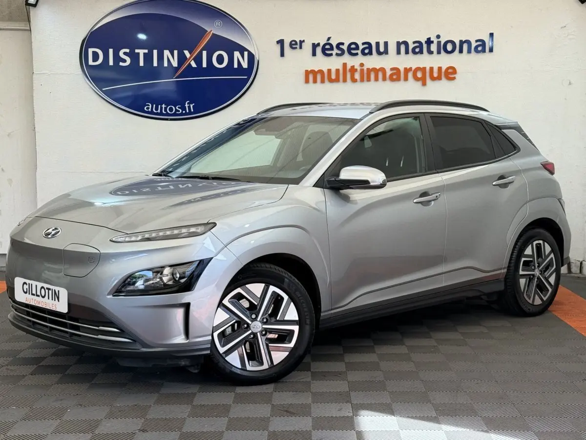 Vue 3/4 avant droite d'un Hyundai Kona électrique gris clair avec jantes spécifiques et rétroviseurs chromés.