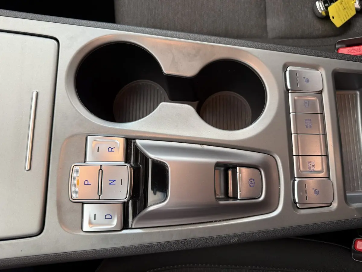 Gros plan sur la console centrale grise du Hyundai Kona électrique 2022 avec boutons de boîte auto et porte-gobelets.
