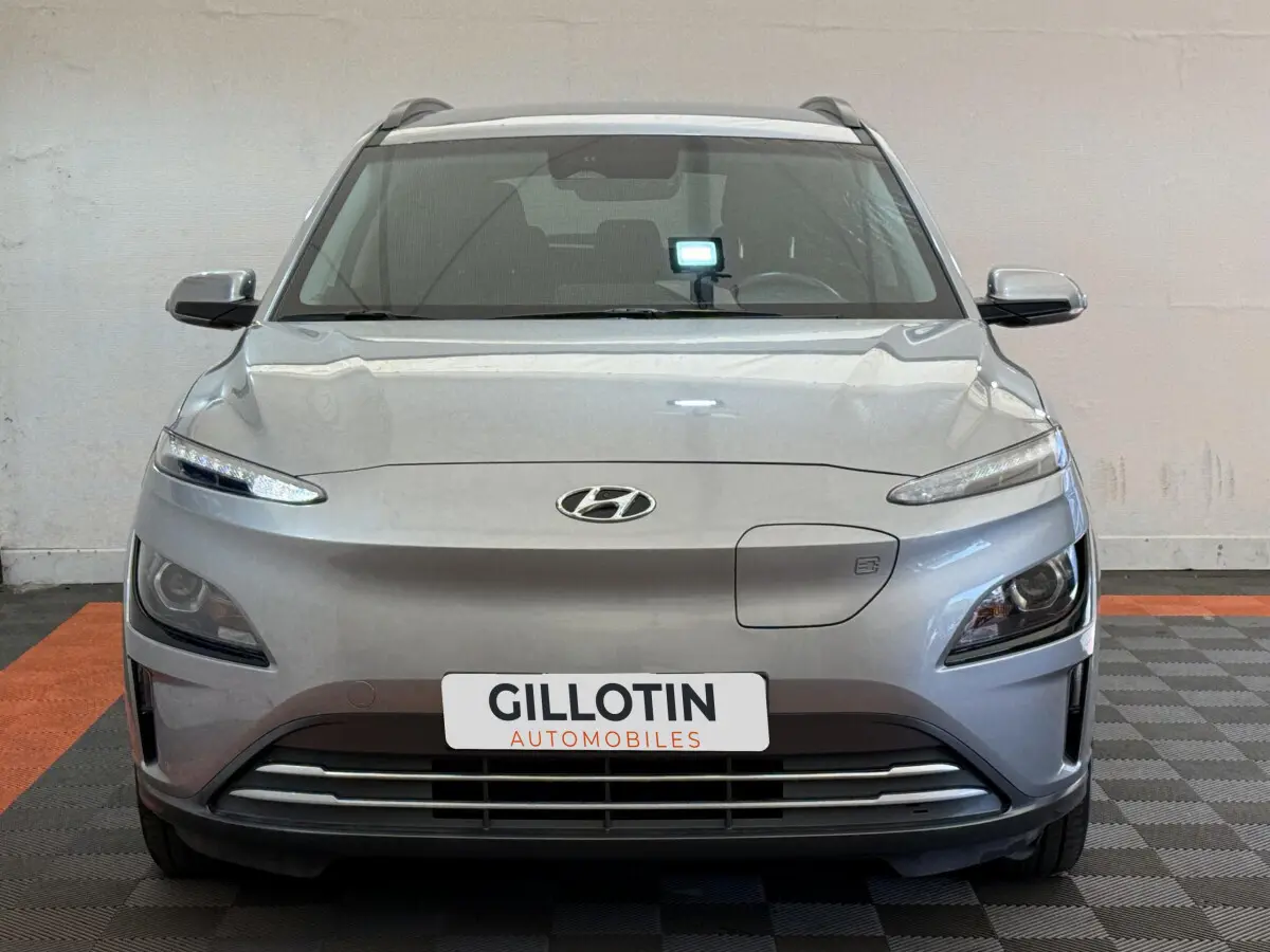 Vue de face du Hyundai Kona électrique gris clair avec phares LED et calandre épurée en intérieur showroom.