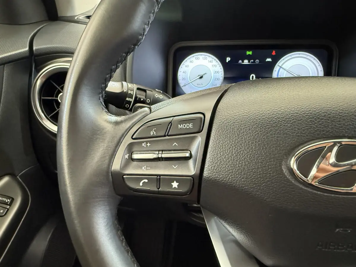 Gros plan sur le volant cuir noir du Hyundai Kona électrique 2022 avec commandes audio et tableau de bord numérique.