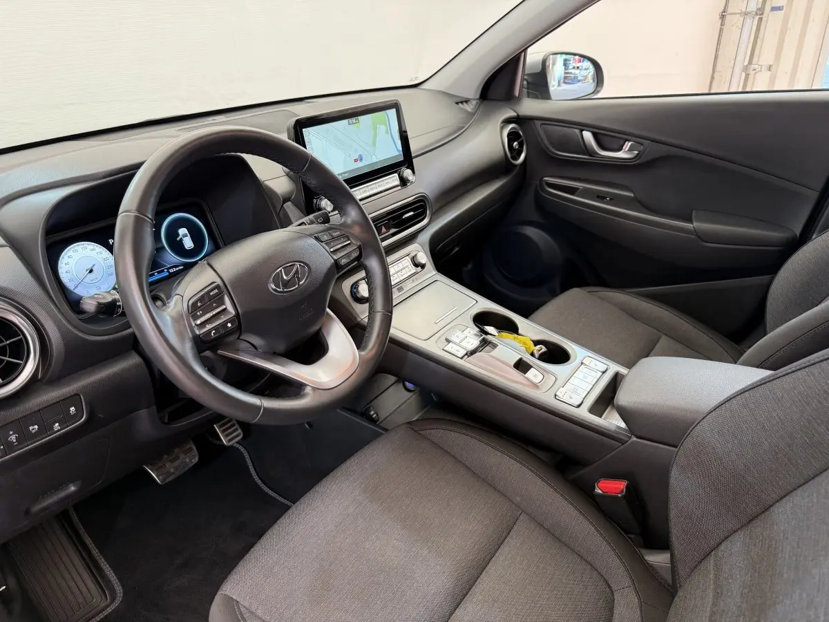 Intérieur côté conducteur du Hyundai Kona électrique 2022, tableau de bord noir avec écran tactile et volant cuir multifonctions.