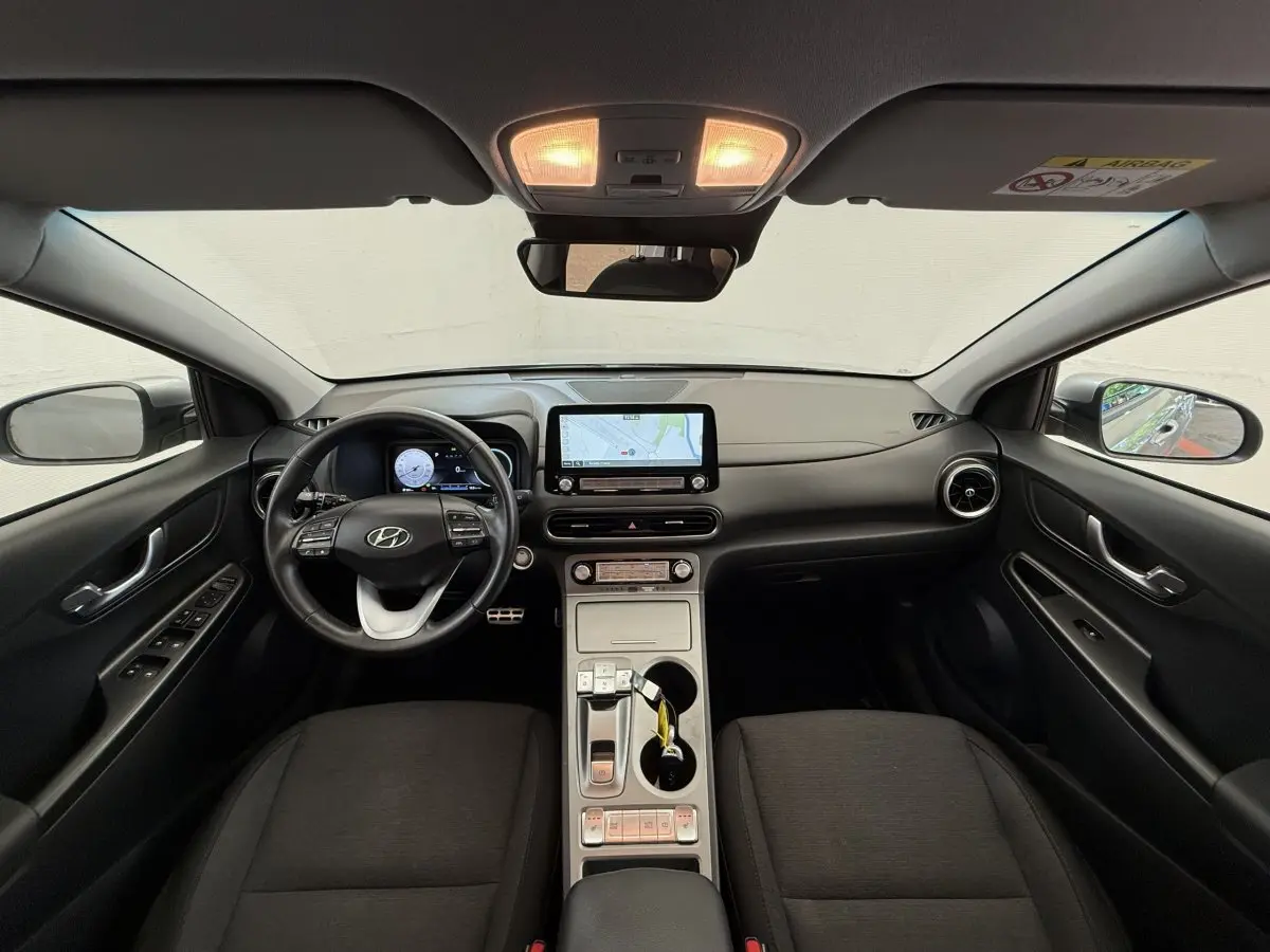 Vue intérieure avant du Hyundai Kona gris clair 2022, tableau de bord moderne avec écran tactile central et volant multifonctions cuir.