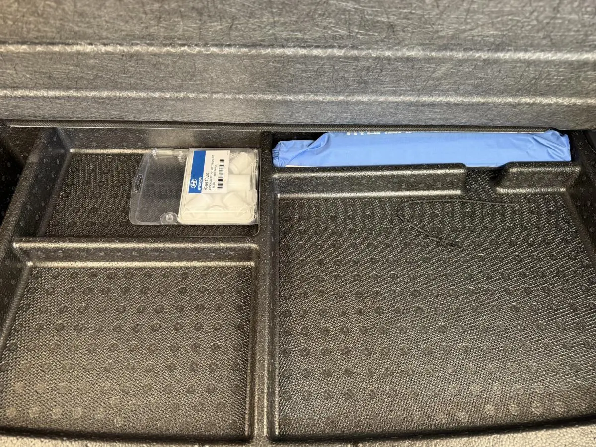 Rangement sous tablette de coffre Hyundai Kona gris clair 2022 avec kit de réparation pneus et trousse bleue.