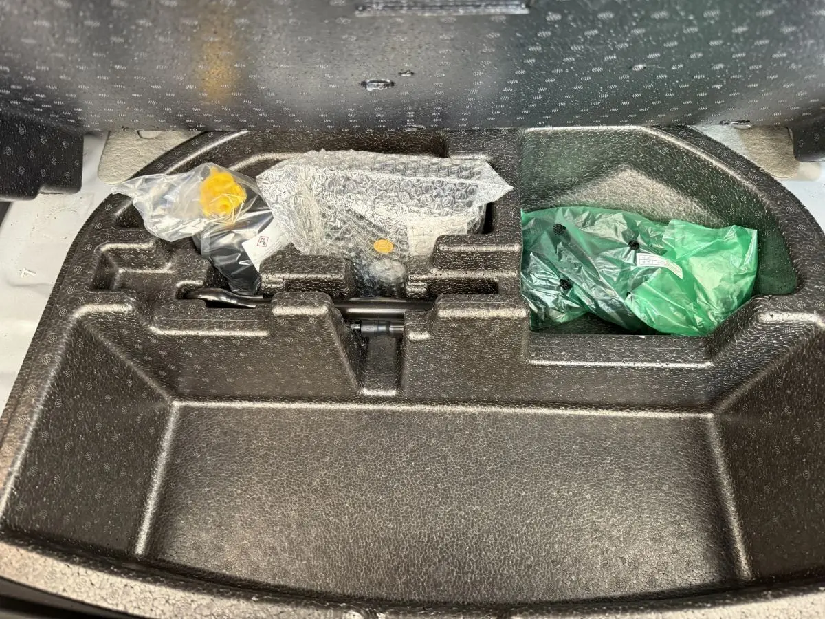 Compartiment de rangement sous le plancher du coffre du Hyundai Kona électrique gris clair, avec outils emballés visibles.