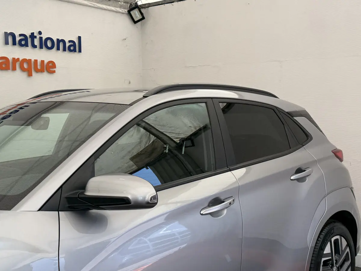 Vue côté gauche du Hyundai Kona électrique gris clair 2022, mettant en valeur les rétroviseurs et les poignées de porte chromées.