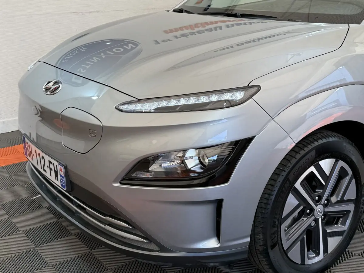 Vue 3/4 avant droit du Hyundai Kona gris clair électrique, mettant en valeur ses phares LED et jante spécifique.