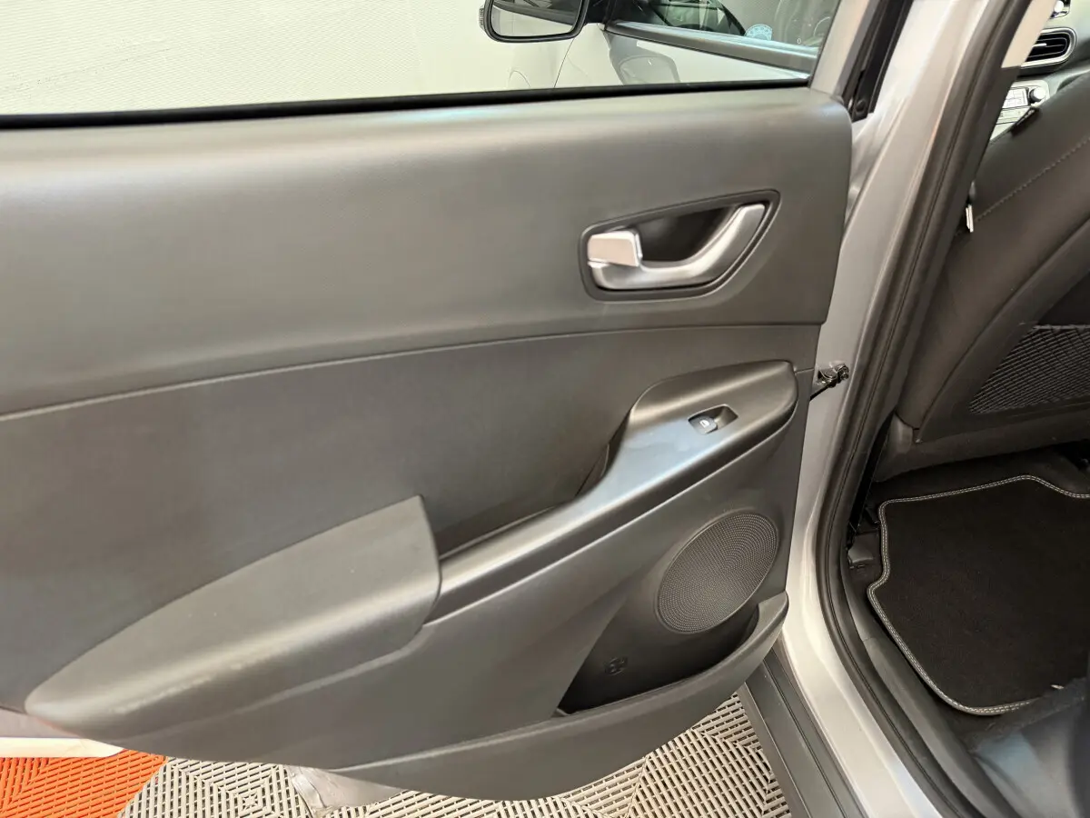 Porte arrière droite ouverte du Hyundai Kona gris clair, montrant la garniture intérieure noire avec poignée et commande de vitre.