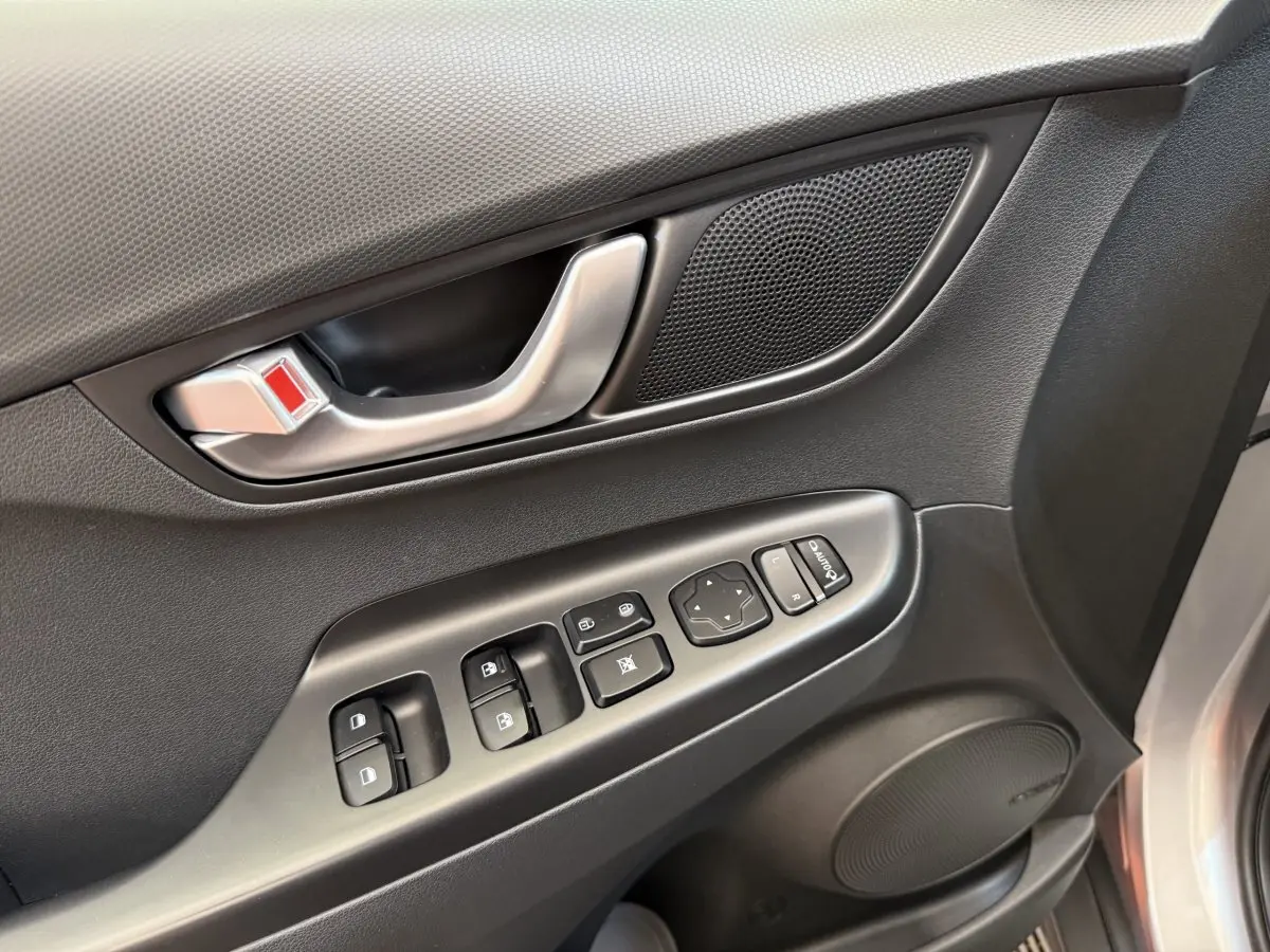 Gros plan sur la porte côté conducteur gris clair du Hyundai Kona électrique, montrant les commandes des vitres et le haut-parleur.