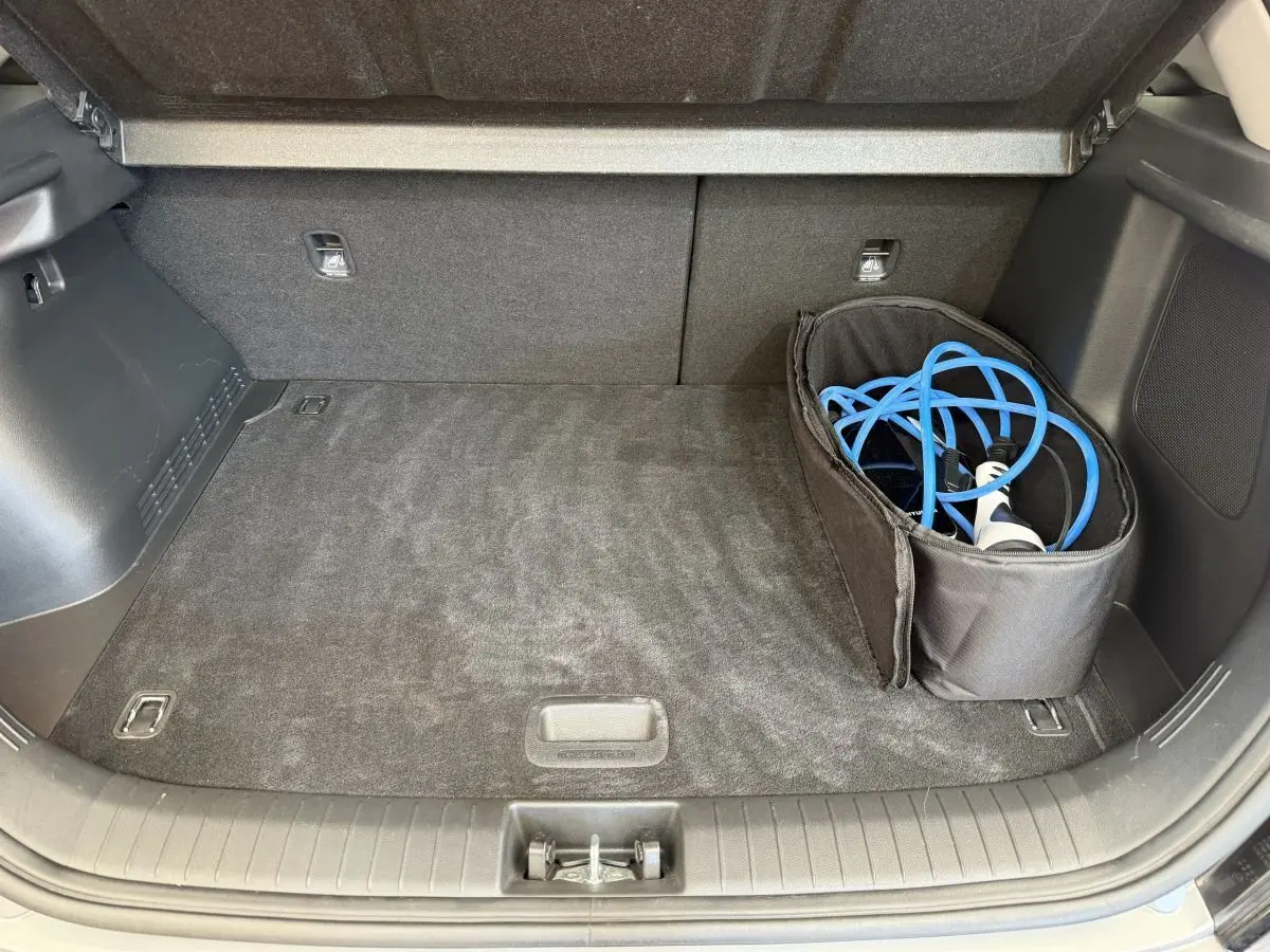 Coffre ouvert du Hyundai Kona électrique gris clair avec câble de recharge bleu rangé dans un sac noir.
