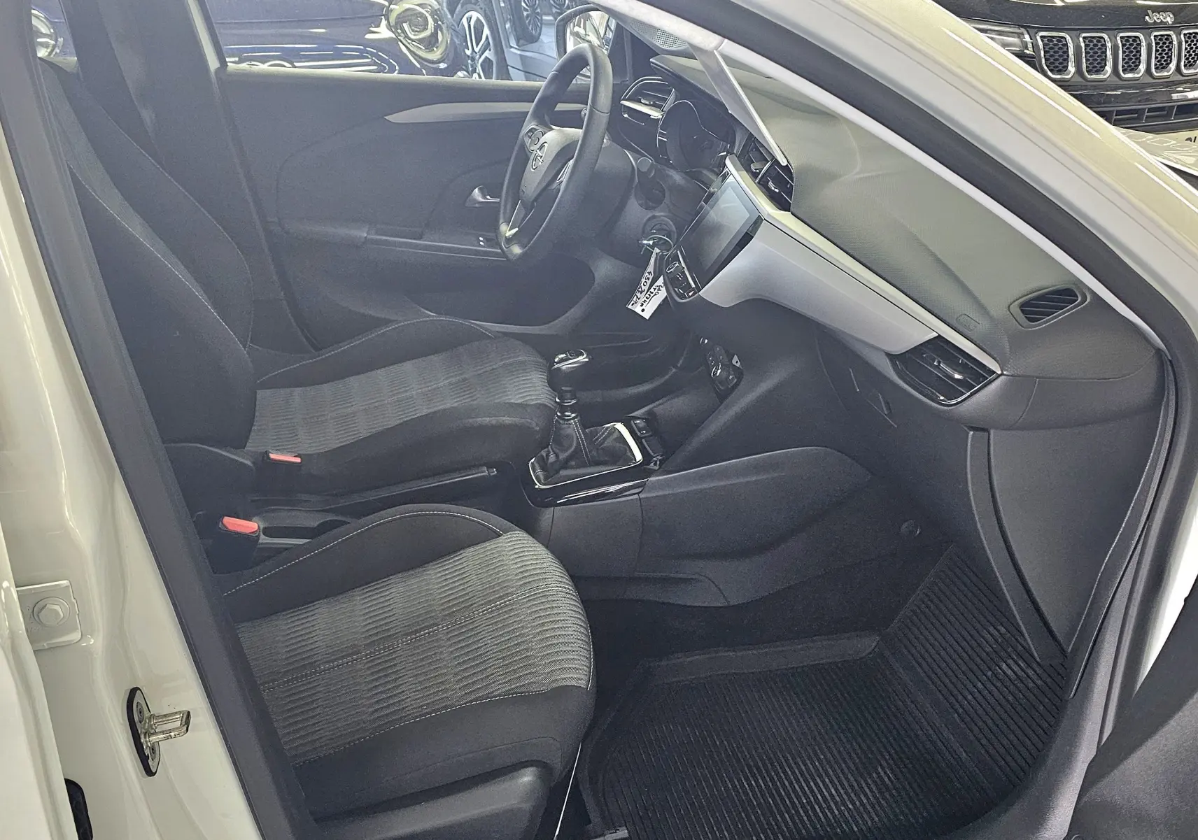 Vue intérieure côté conducteur de l'Opel Corsa blanc glacier 2022, montrant sièges tissu gris et tableau de bord moderne.