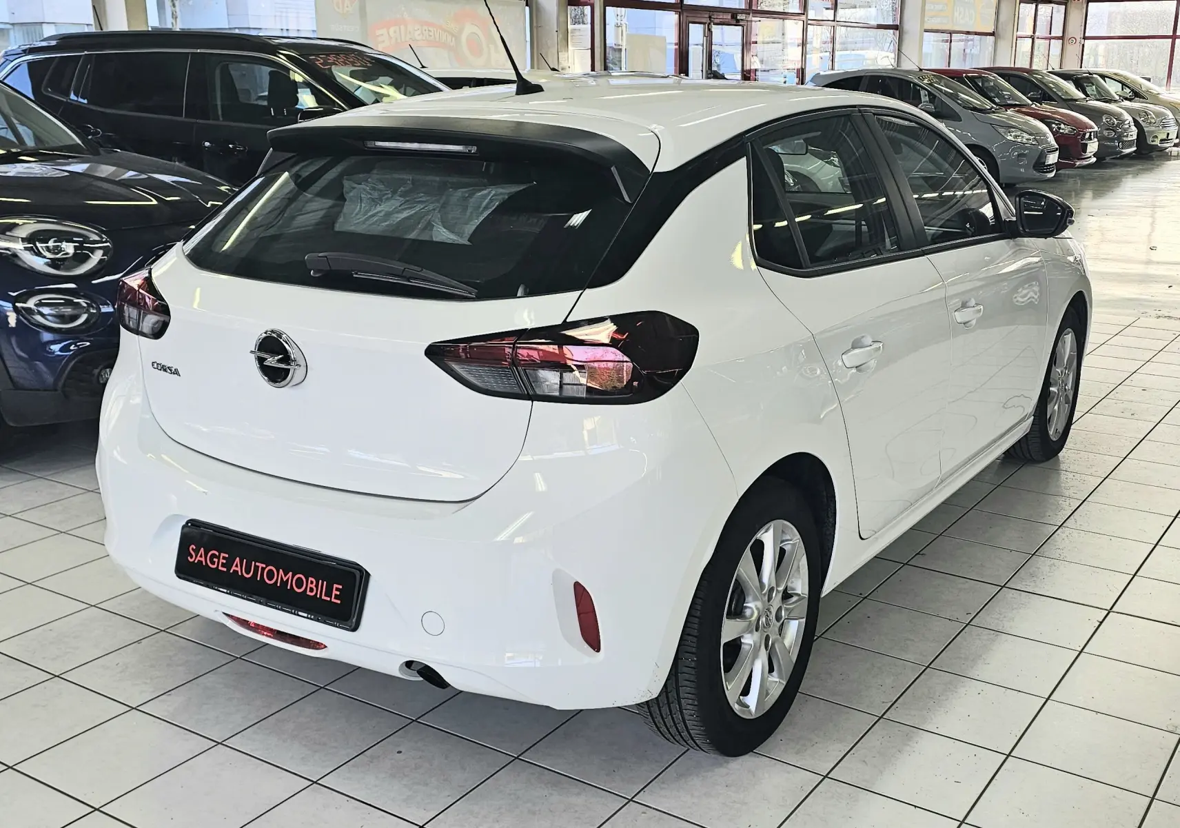 Vue 3/4 arrière droite d'une Opel Corsa blanche glacier 5 portes, avec feux arrière foncés et jantes alliage en showroom.