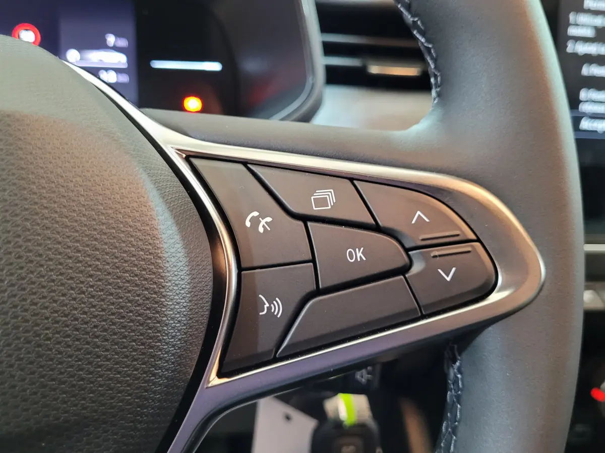 Gros plan sur les commandes multifonctions à droite du volant cuir de la Renault Clio bleu 2025.