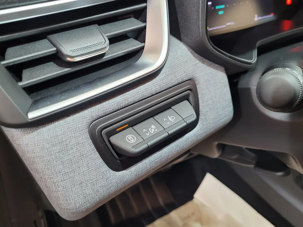 Gros plan sur les commandes d'éclairage et verrouillage à gauche du tableau de bord gris clair de la Renault Clio bleue 2025.