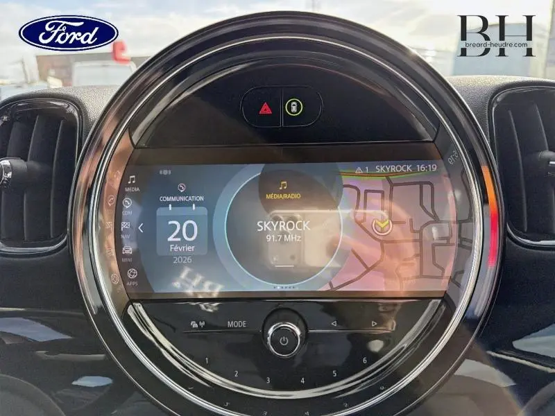 Vue rapprochée de l’écran tactile central rond du MINI Countryman 2023 en Melting Silver III avec interface GPS et radio Skyrock.
