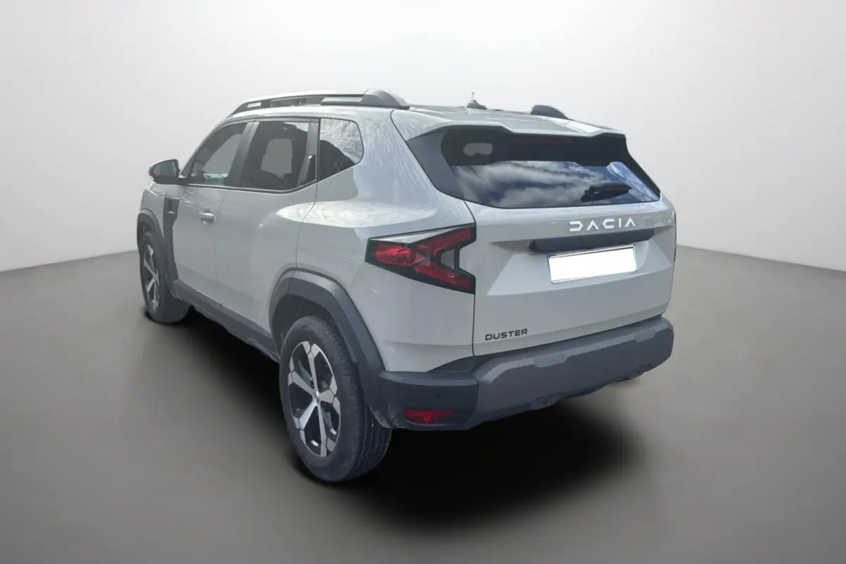 Vue 3/4 arrière gauche d'un Dacia Duster 2025 couleur Sandstone avec jantes alu 18 pouces et barres de toit.