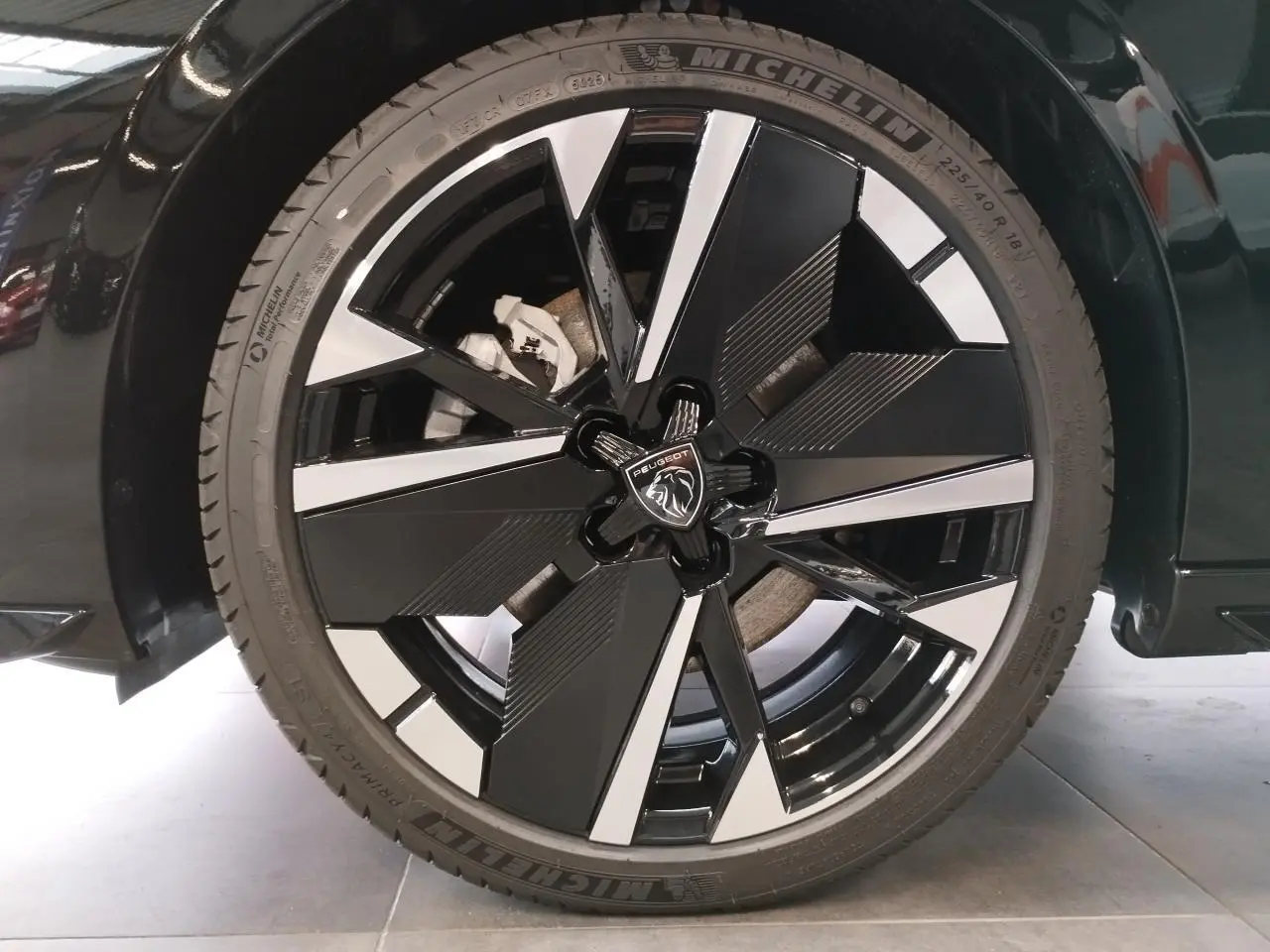 Gros plan sur la jante alliage 18 pouces bi-tons noir et argent avec logo Peugeot au centre, sur carrosserie noire métallisée.