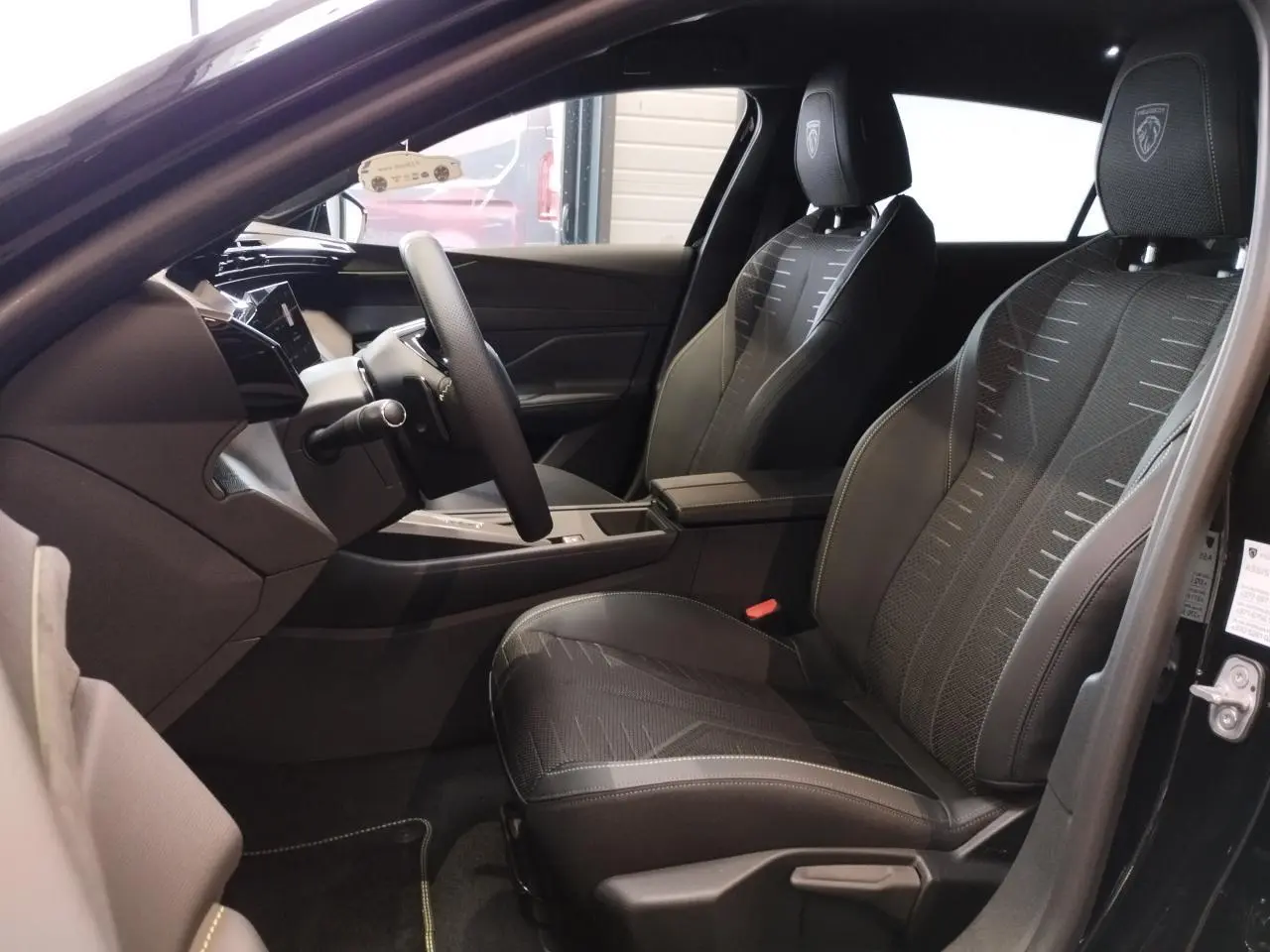 Vue intérieure côté conducteur de la Peugeot 308 hybride 2026 noire, sièges tissu noir avec surpiqûres vert Adamite.
