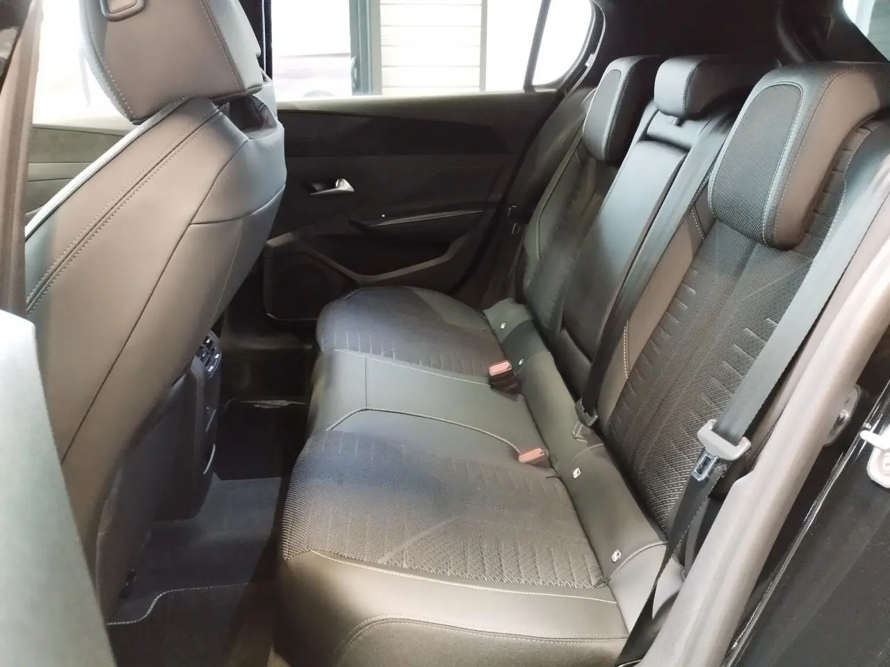 Vue intérieure côté droit montrant la banquette arrière noire avec surpiqûres vert Adamite sur Peugeot 308 Hybrid 2026.