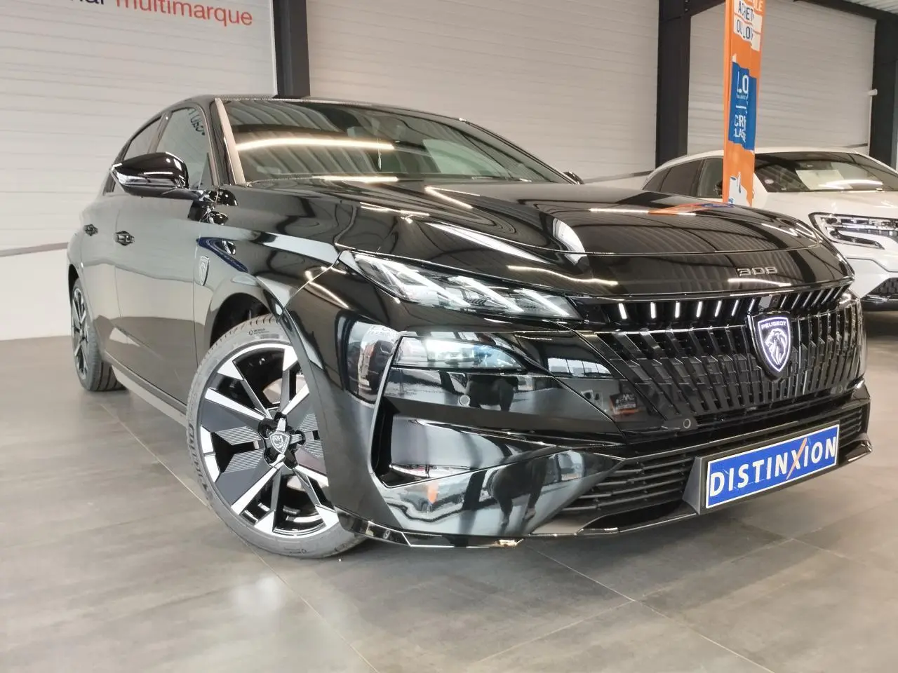 Peugeot 308 noir métal vue 3/4 avant avec calandre distinctive et jantes alliage bi-tons dans un showroom.