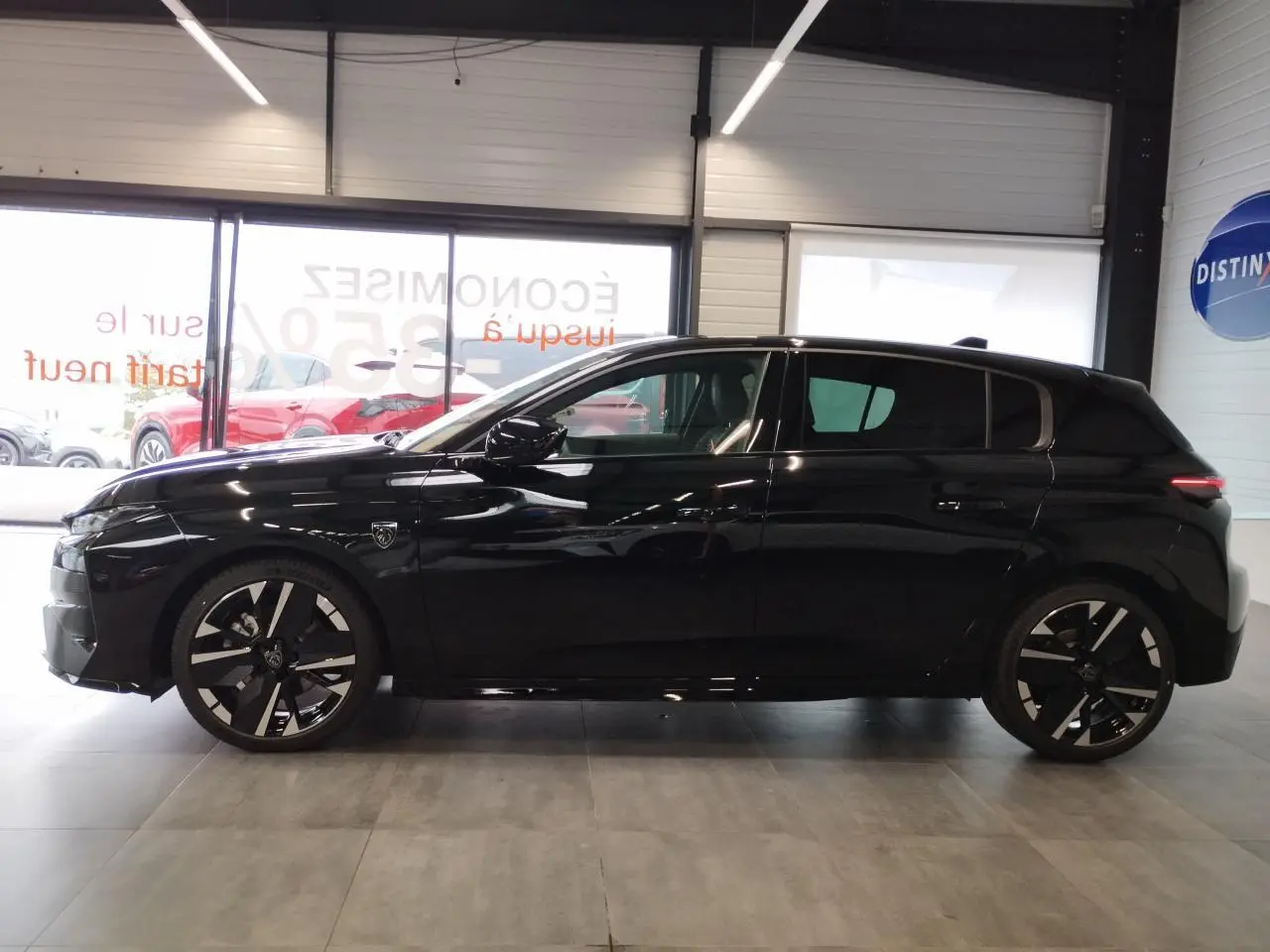 Peugeot 308 1.2i Hybrid noire métallisée vue de profil côté gauche, avec jantes alliage bi-ton et blason sur aile avant.