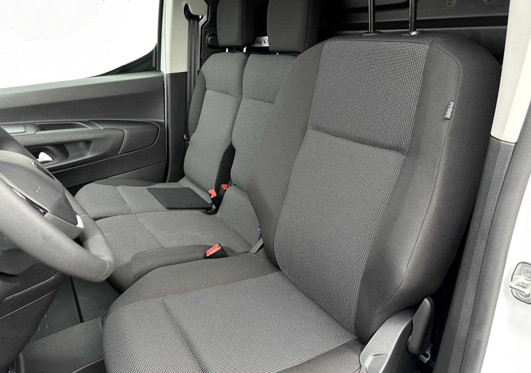 Vue intérieure côté conducteur du Peugeot Partner Fourgon blanc 2024, sièges tissu gris foncé avec appuie-tête intégrés.