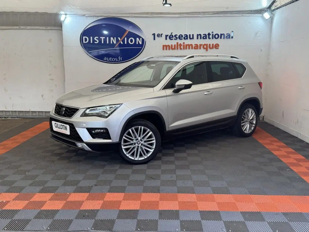 SEAT Ateca gris clair vu en 3/4 avant droit dans un showroom avec sol à damiers gris et orange.