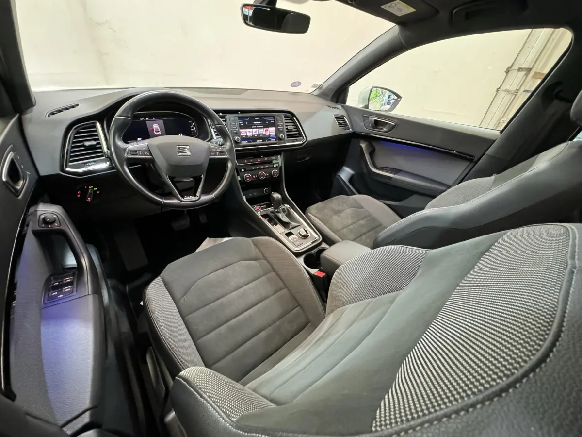Intérieur de la SEAT Ateca vu côté conducteur, sièges gris et tableau de bord avec écran tactile central.