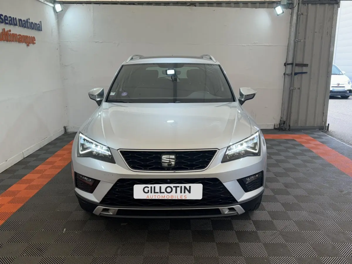 SEAT Ateca gris clair vu de face, phares LED allumés, calandre noire et toit avec barres de toit visibles.