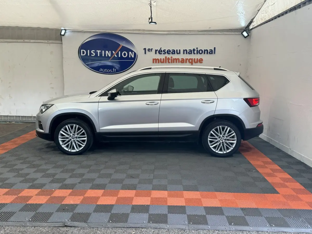 Profil côté gauche d'un SUV SEAT Ateca gris clair 2019 dans un showroom avec sol à damier gris et orange.