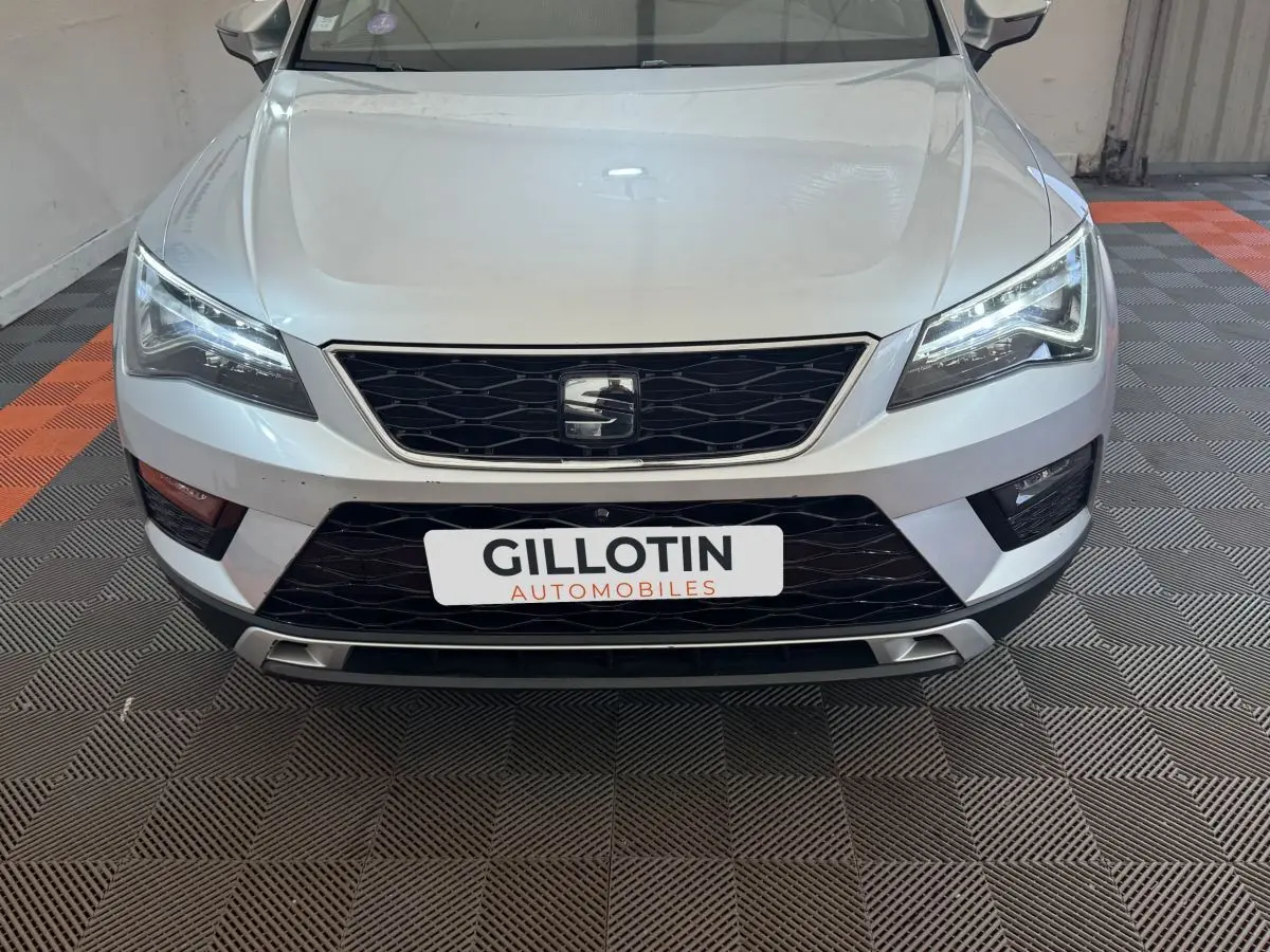 Vue frontale d'un SEAT Ateca gris clair avec phares LED allumés et calandre noire en intérieur showroom.