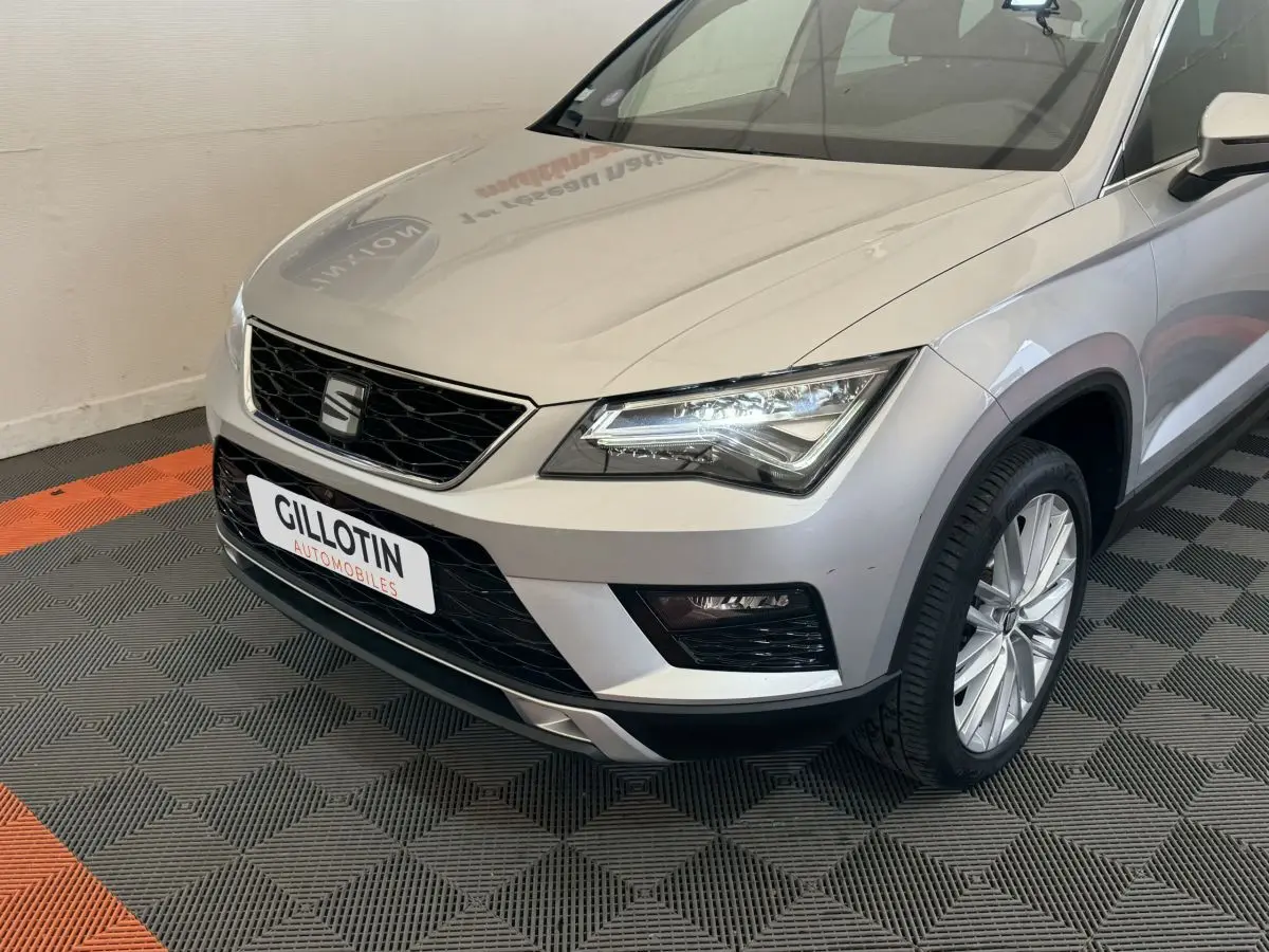 Vue 3/4 avant droit d'un SEAT Ateca gris clair avec phares LED et calandre noire en intérieur showroom.