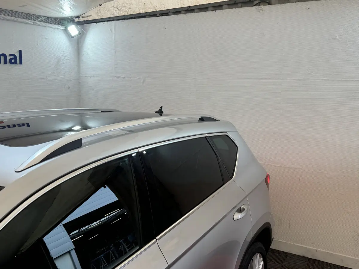 Vue côté droit arrière d'un SUV SEAT Ateca gris clair avec barres de toit et vitres teintées dans un garage.