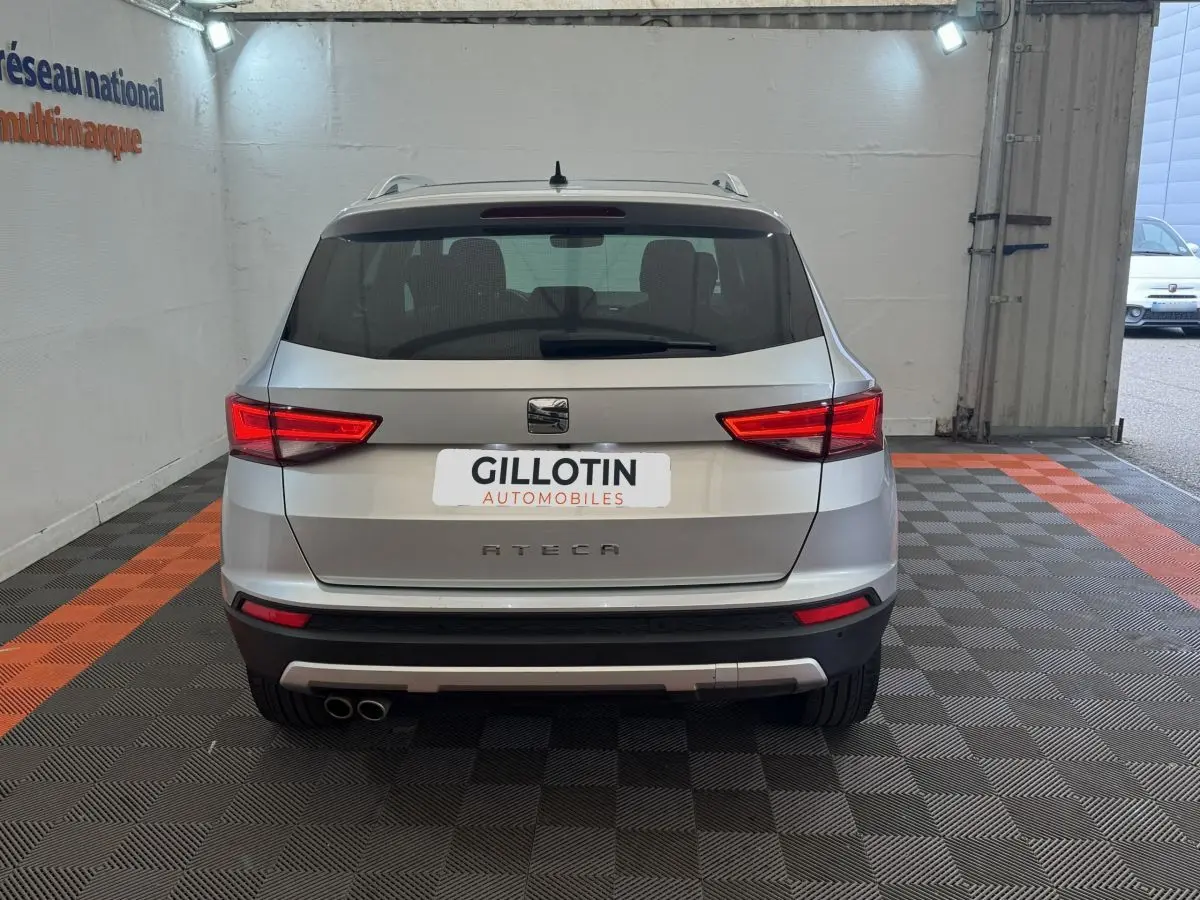 Vue arrière d'un SEAT Ateca gris clair stationné en intérieur avec feux arrière allumés et double sortie d'échappement visible.
