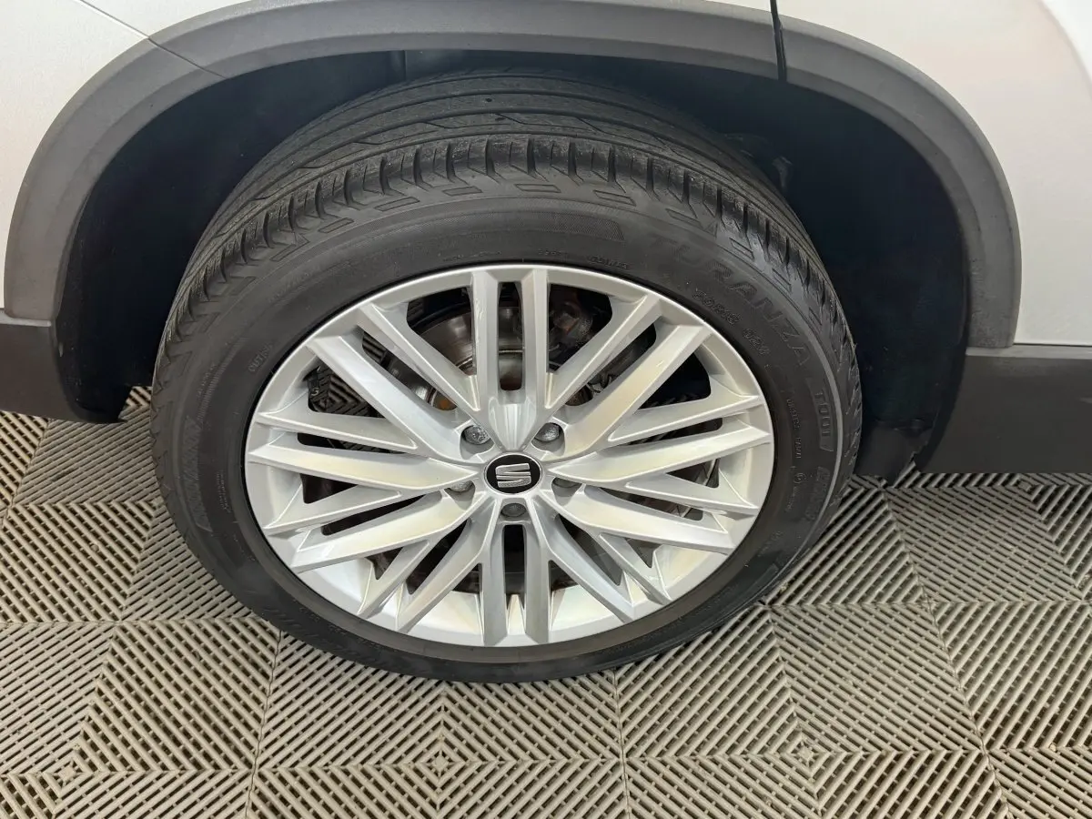 Gros plan sur la roue avant droite du SEAT Ateca gris clair, avec jante alliage à rayons fins et logo central.