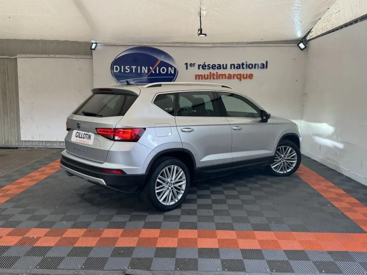 SEAT Ateca gris clair vu de trois quarts arrière droit dans un showroom avec logo Distinxion en arrière-plan.