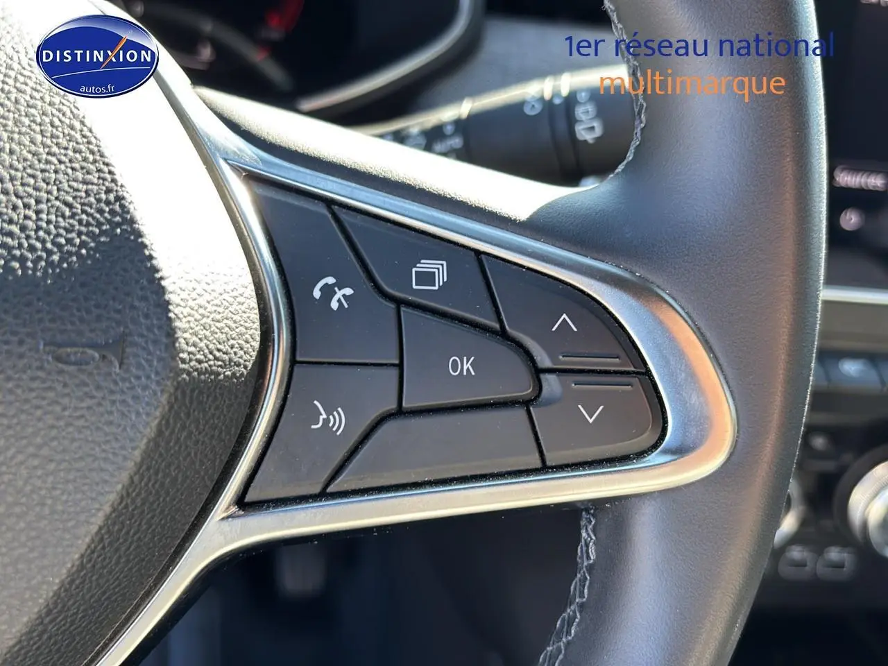 Gros plan sur les commandes multifonctions gauche du volant textile enduit gris de la Renault Clio V 2024.