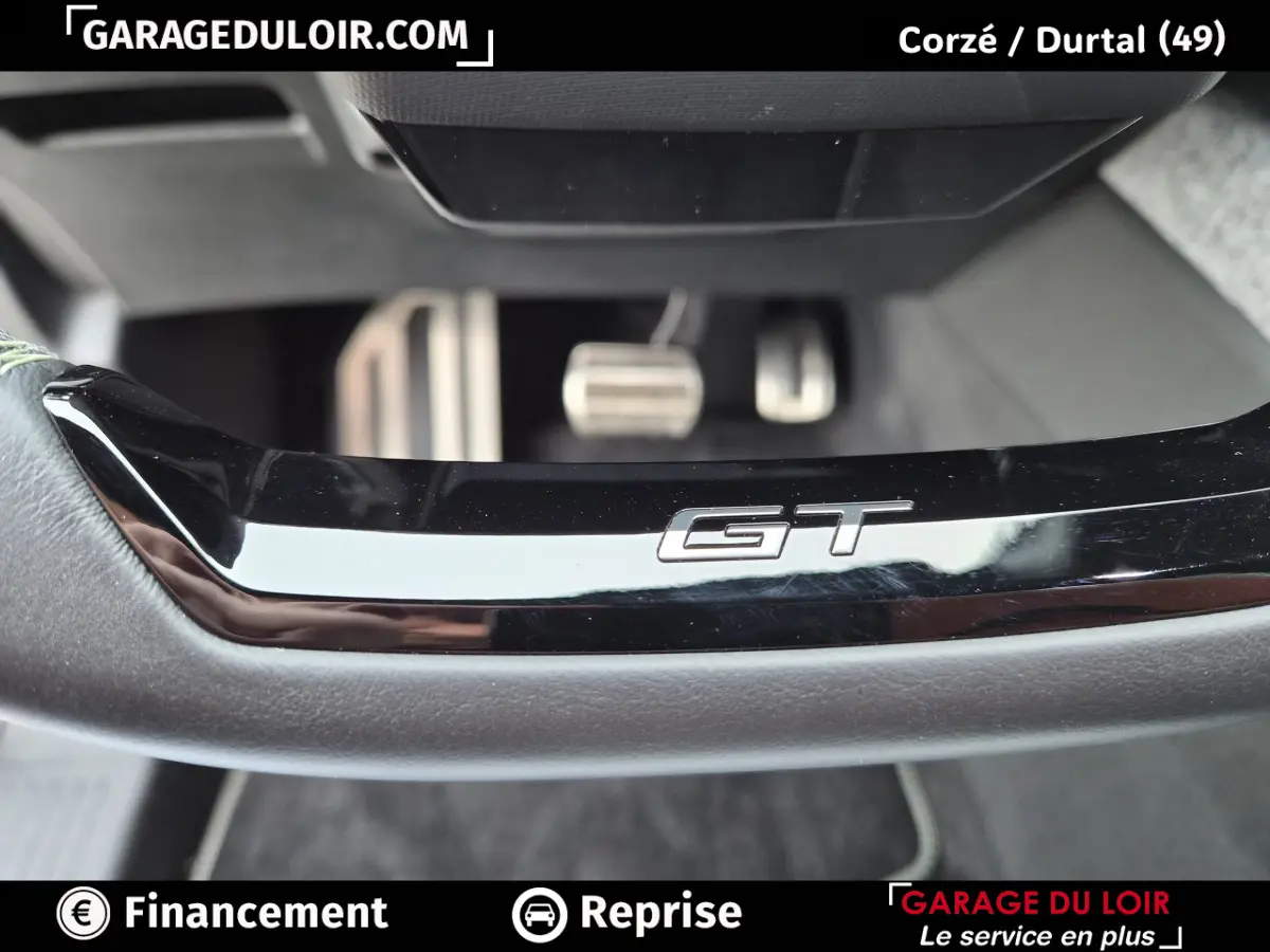 Gros plan sur le bas du volant noir avec logo GT et pédales en aluminium du Peugeot 3008 blanc 1.2 Hybrid 145 GT.