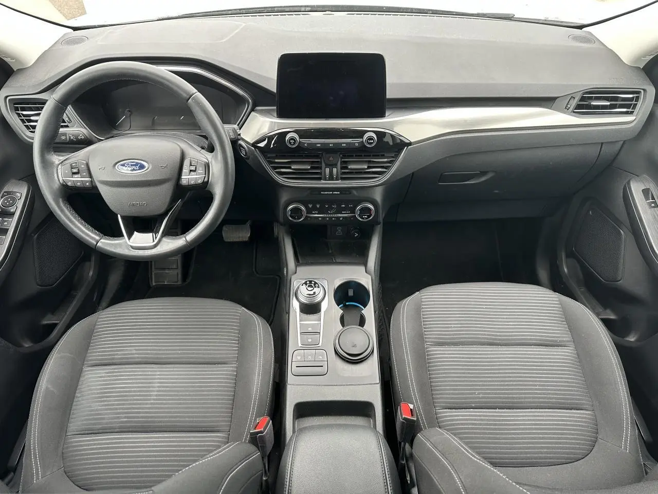 Intérieur avant du Ford Kuga gris solaire 2020, vue centrée sur le tableau de bord, volant multifonctions et console centrale avec sélecteur rotatif.