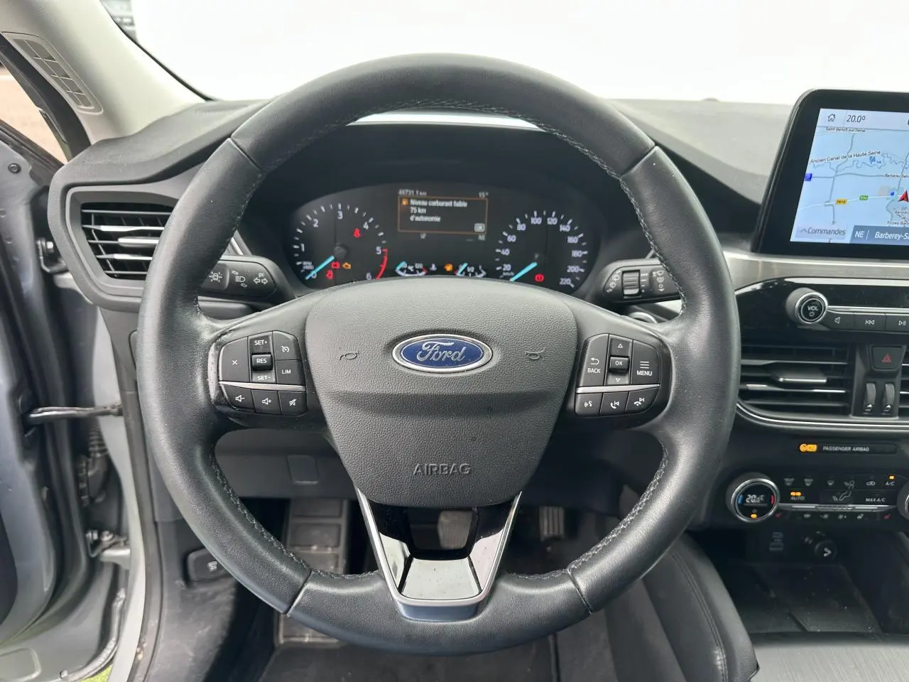 Vue intérieure centrée sur le volant cuir noir et le tableau de bord du Ford Kuga gris solaire 2020 avec écran tactile et commandes intégrées.