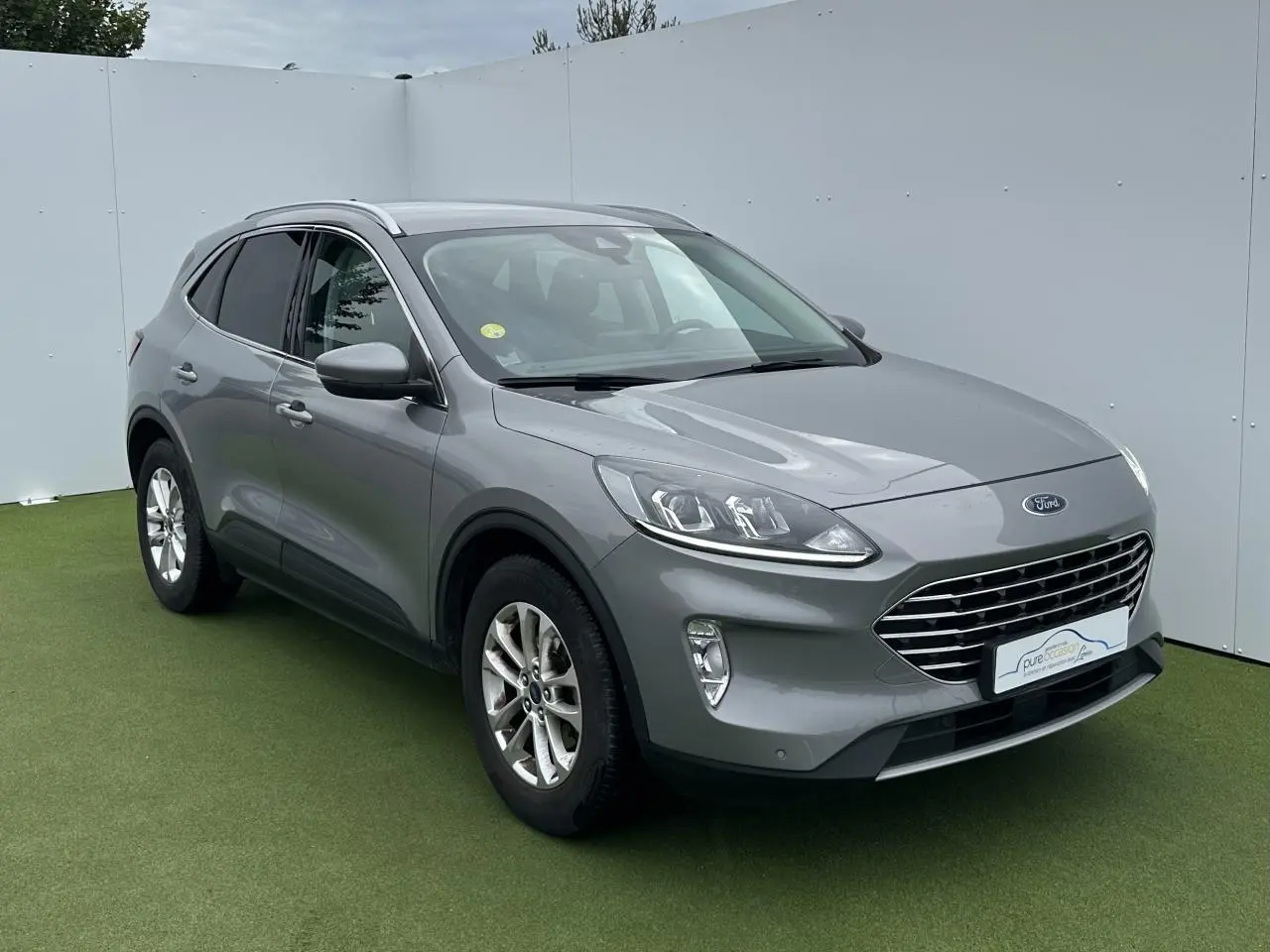 Ford Kuga gris solaire en 3/4 avant droit avec barres de toit aluminium et jantes alliage 17 pouces.