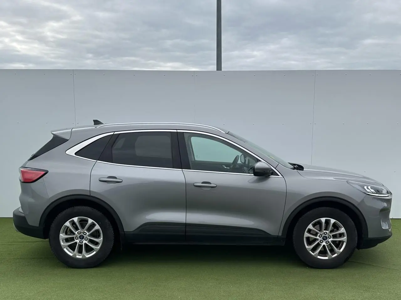 Vue de profil côté gauche du Ford Kuga III gris solaire avec barres de toit aluminium et vitres arrière surteintées.