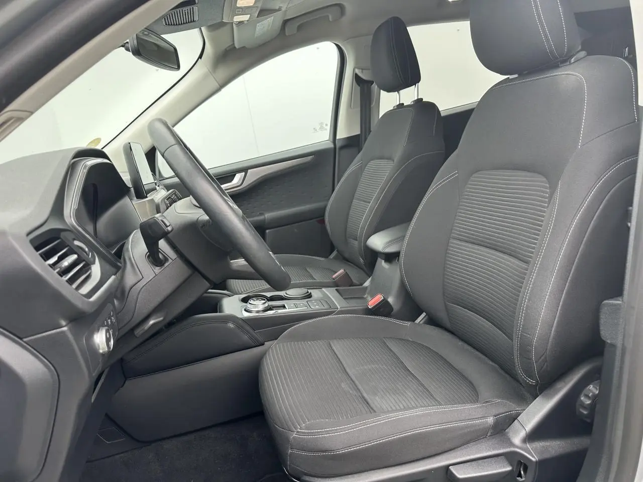 Vue intérieure côté conducteur du Ford Kuga gris solaire 2020, sièges tissu noir et console centrale avec sélecteur rotatif.