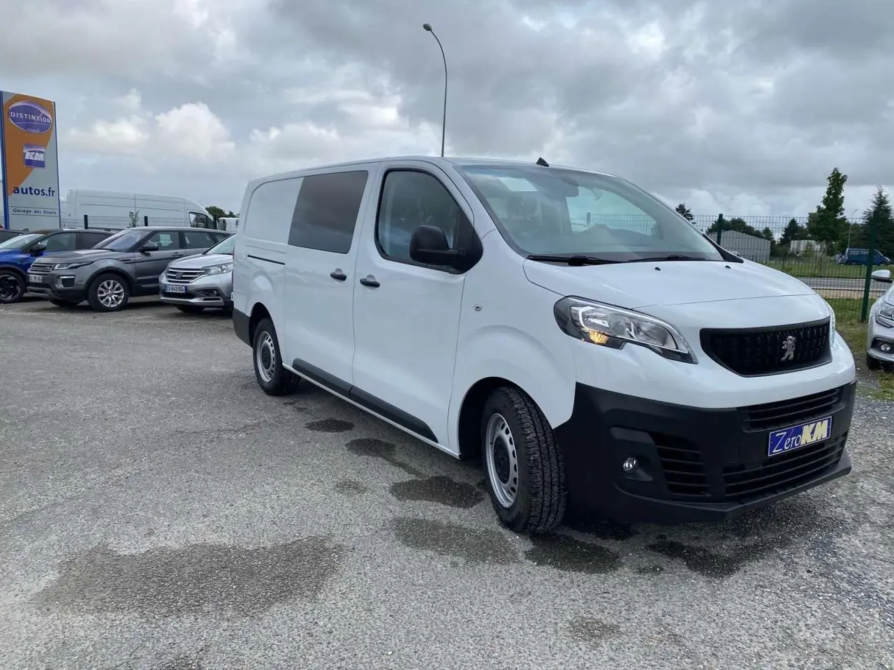 Peugeot Expert Fourgon blanc vu en 3/4 avant droit sur parking avec calandre noire et feux allumés.