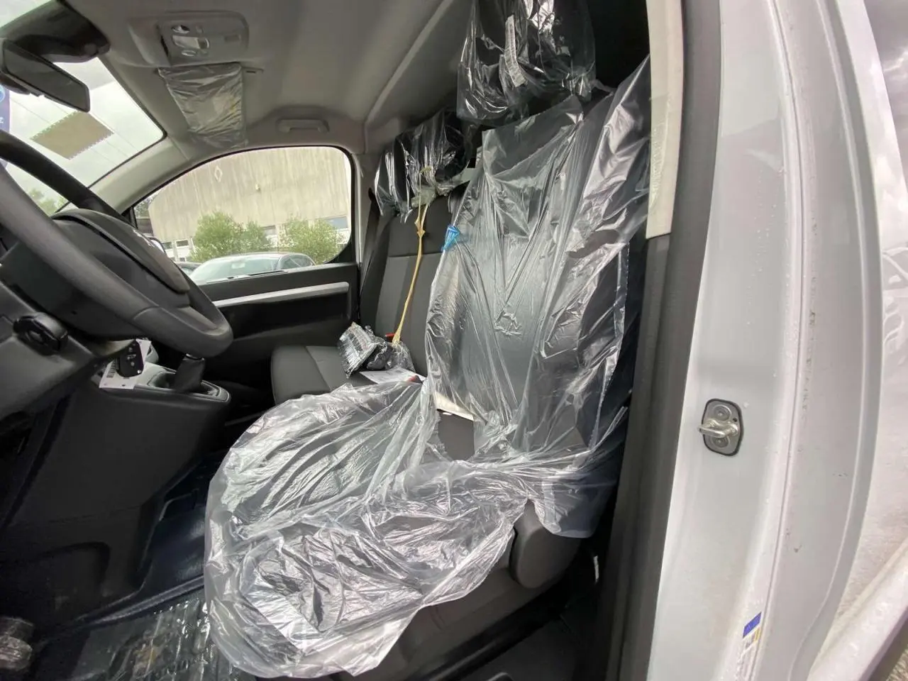 Vue intérieure côté conducteur du Peugeot Expert Fourgon blanc 2023, sièges avant protégés par film plastique.