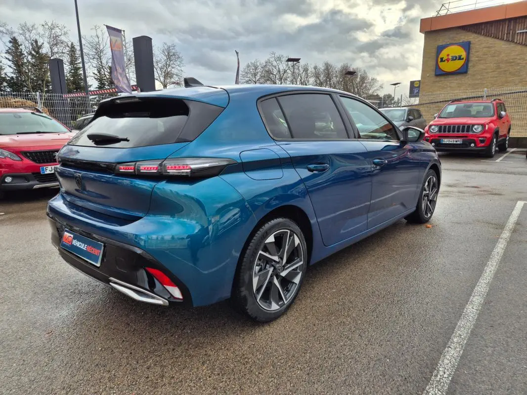 Vue 3/4 arrière droite d'une Peugeot 308 bleu métallisé 2024 avec jantes alliage et feux arrière LED distinctifs.