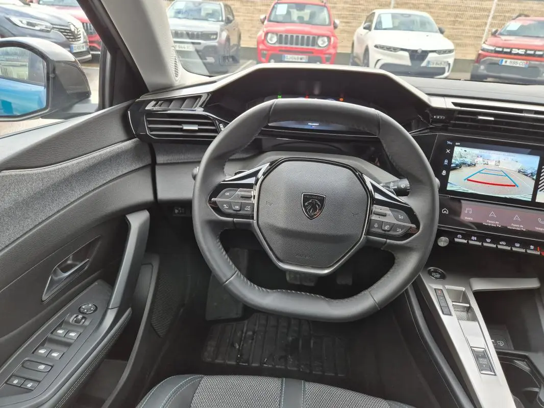 Vue intérieure centrée sur le volant et le tableau de bord numérique de la Peugeot 308 bleu avec caméra de recul affichée.