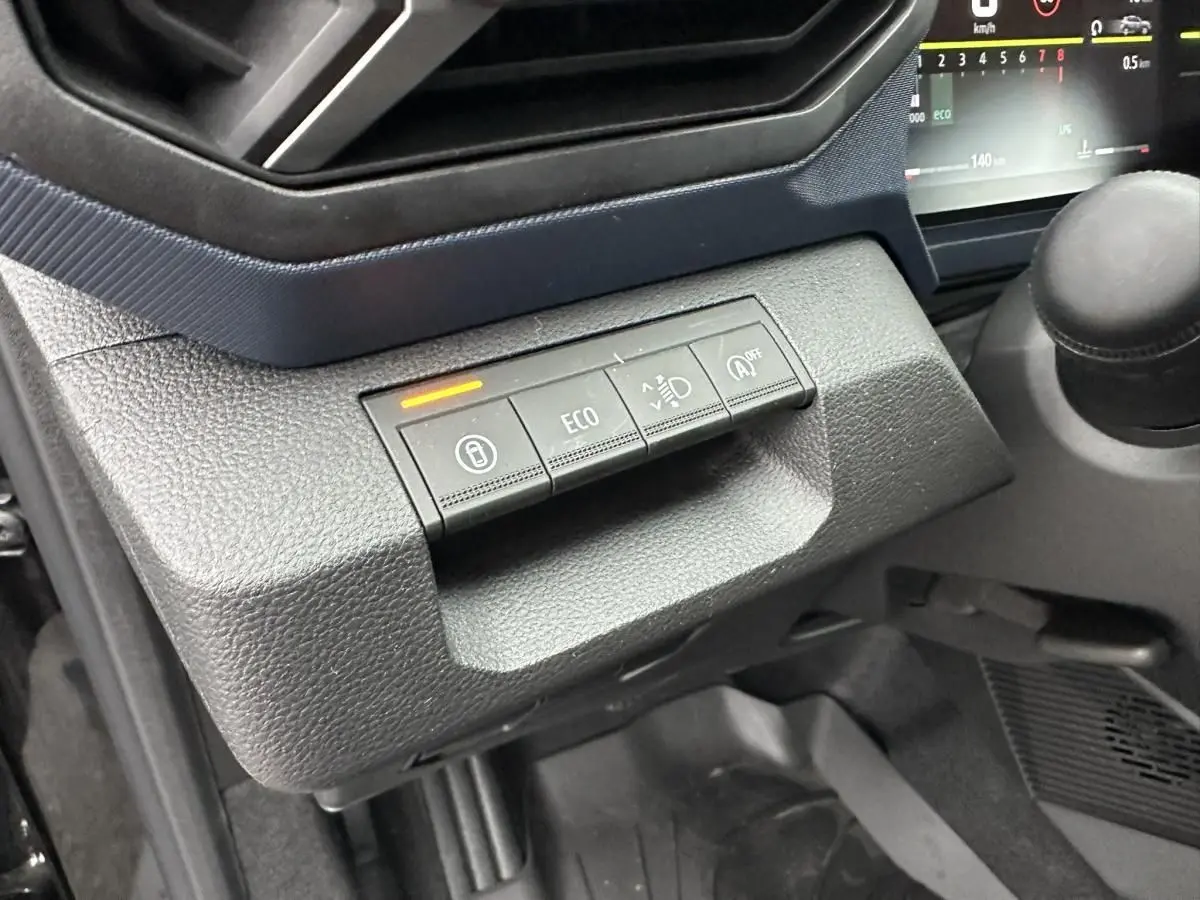 Gros plan sur les commandes de tableau de bord du Dacia Duster noir 2025, avec bouton ECO et indicateur lumineux orange.