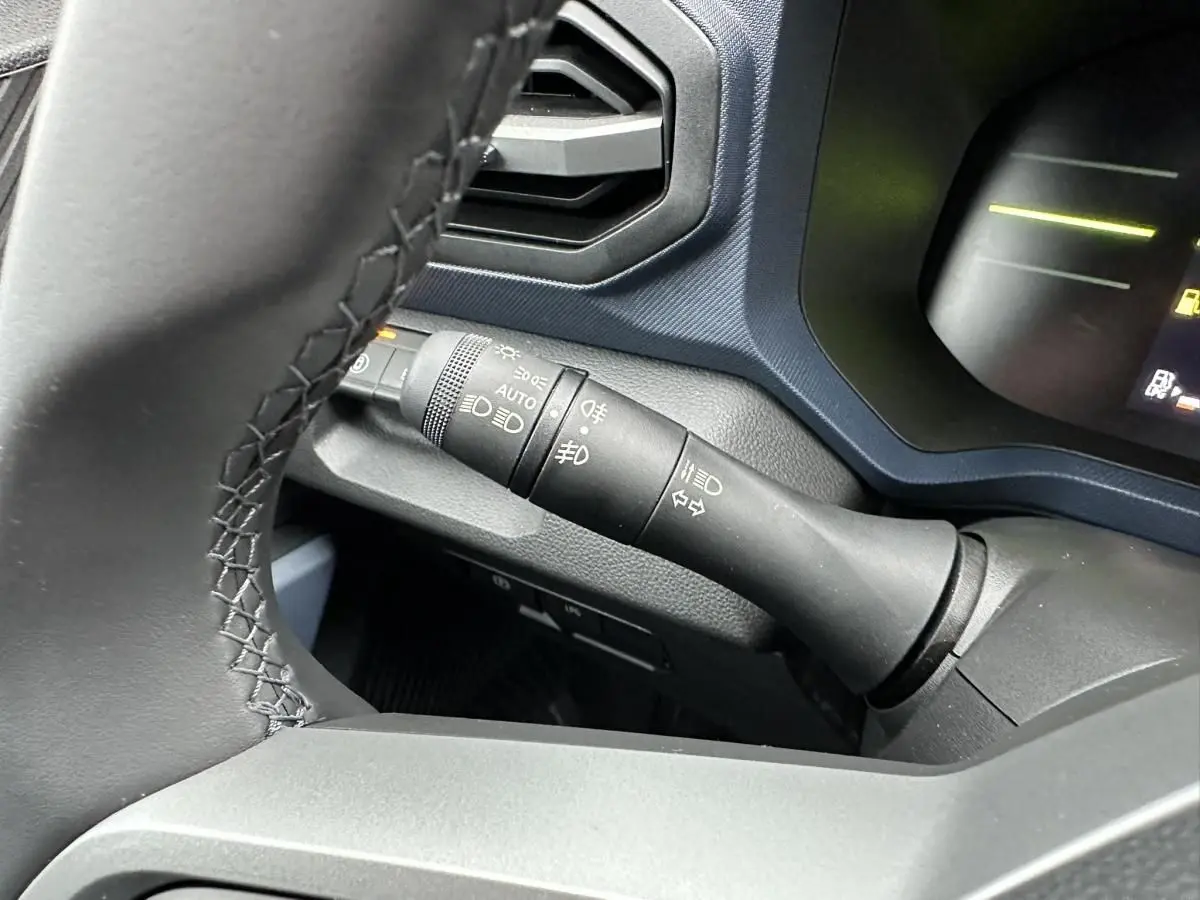 Gros plan sur la commande des feux et clignotants à gauche du volant dans le Dacia Duster noir 2025.