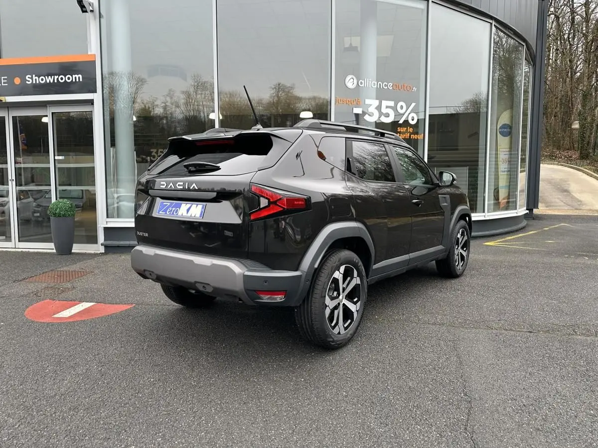 Vue 3/4 arrière droite du Dacia Duster noir métallisé 2025 avec jantes alliage 18” et barres de toit longitudinales.