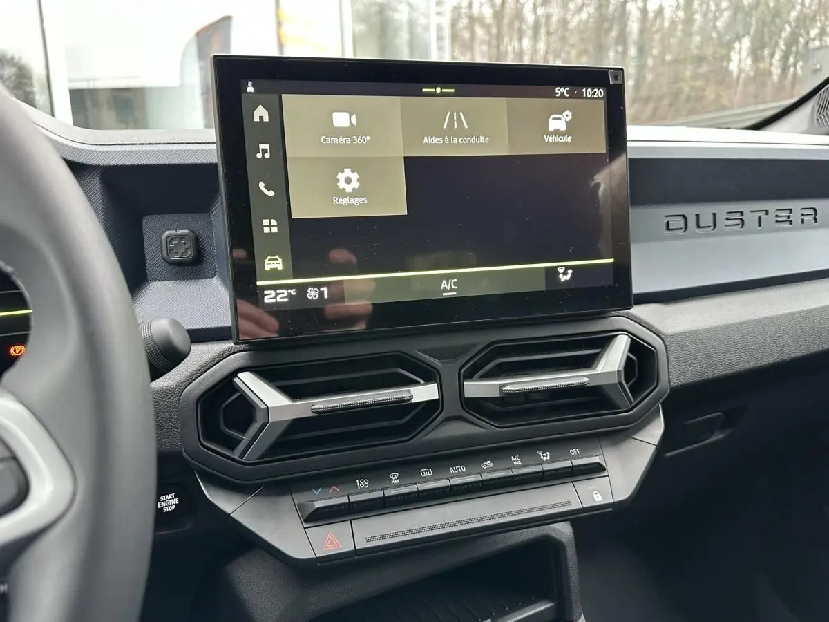 Vue intérieure du tableau de bord du Dacia Duster 2025 noir, avec écran tactile central et aérateurs hexagonaux.